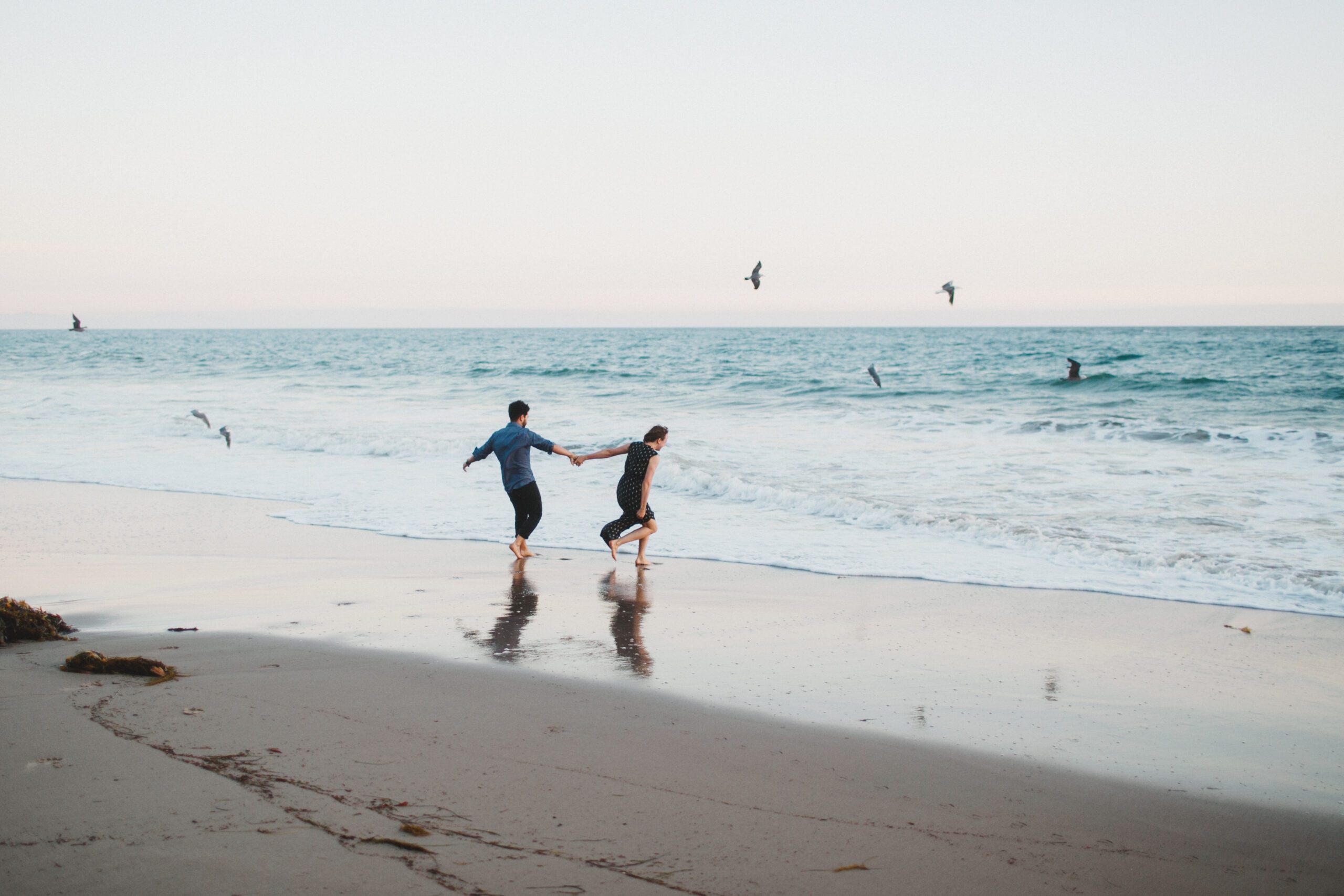 Naples Florida Engagement Session with a couple holding hands running toward the ocean and birds flying in the background