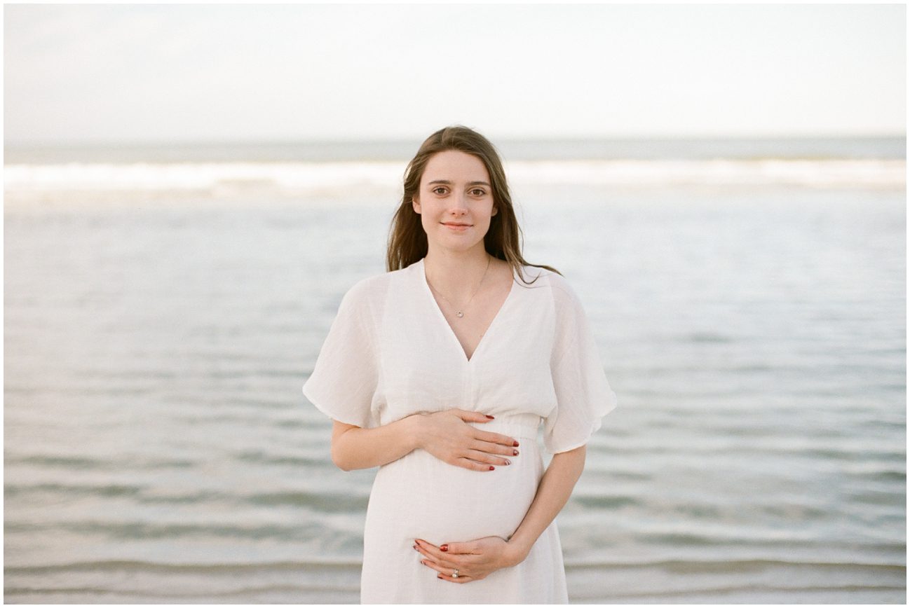 photo of a pregnant woman in a white dress with the Gulf behind her taken for a maternity session in Naples Florida